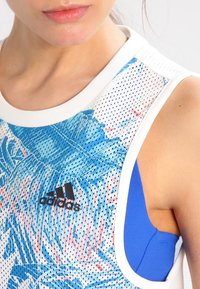 Sportovní tílko s modro-bílým vzorem listů a síťovanou strukturou, černým logem Adidas a bílým žebrovaným výstřihem, navrženo pro sportovní nošení.