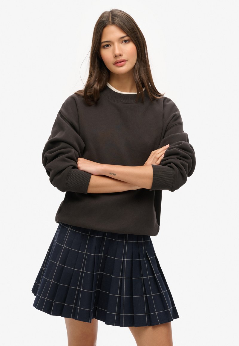 Dunkelgraues, übergroßes Sweatshirt mit gerippten Bündchen, kombiniert mit einem marineblauen, gefältelten Rock mit einem hellen Karomuster.
