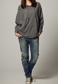 Šedá oversized mikina s kapucí a šňůrkami, v kombinaci s vybledlými modrými džíny a světlými teniskami. Neformální a pohodlný střih.