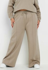 Beige vida byxor i mjukt tyg med elastisk midja och snörning. Har vertikala sömmar och en avslappnad passform.