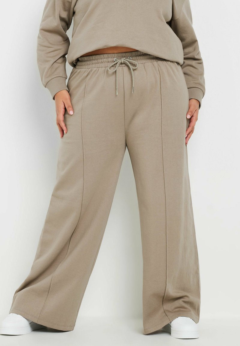 Beige vida byxor i mjukt tyg med elastisk midja och snörning. Har vertikala sömmar och en avslappnad passform.