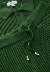 Polo en maille texturée verte avec col, patte de boutonnage et detail de cordon sur les poignets et l'ourlet côtelés.