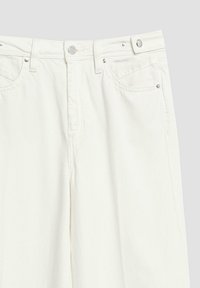 Jean en denim blanc vue de face avec bouton métallique, fermeture éclair, passants de ceinture et poches avant avec rivets sur un fond uni.