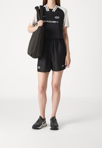 Svartvit sportoutfit med en kortärmad tröja med ränder och logotyp, kombinerad med svarta shorts och mörka sportskor.