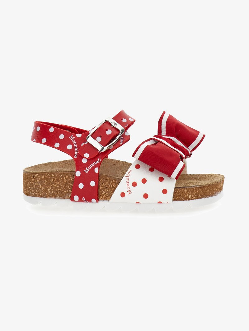 Punane ja valge täpiline sandaal, millel on korkpõhi; omaduseks reguleeritav rihm metallehe ja dekoratiivne pael.