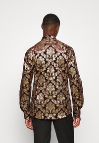 Bordová košile se zlatým damaskovým vzorem, dlouhými rukávy a vysokým límcem, vyrobená z hladké, lesklé látky.