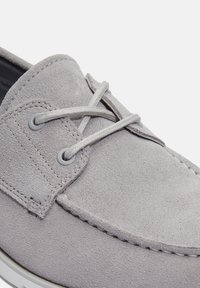 Scarpa da barca in suede grigio con lacci rotondi, occhielli grigi e cuciture a contrasto. Presenta una suola in gomma liscia e una silhouette classica.