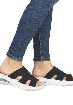 Black mesh slide sandals with white thick soles featuring cut-out designs. Worn with slim-fit blue denim jeans.