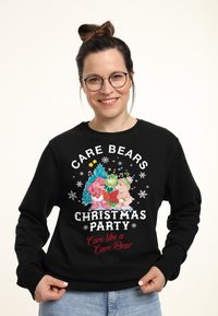 Felpa nera con una grafica colorata del party di Natale dei Care Bears, che include personaggi, fiocchi di neve e testo. Tessuto morbido, colletto a girocollo.