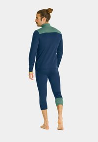 Navy long-sleeve top features a green collar and upper back design; matching navy leggings with green accents at the cuffs. Smooth fabric texture.