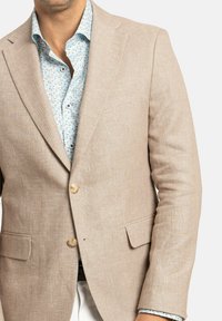 Blazer de lino beige con dos botones, solapas de muesca y bolsillos laterales, superpuesto sobre una camisa azul clara con un patrón floral.