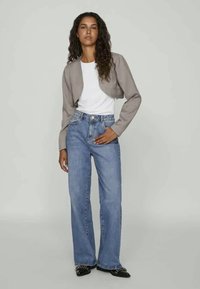 Pelēka saīsināta jaka virs baltā t-krekla, apvienota ar augstā vidukļa ziliem džinsiem. Melni apavi ar metāliskām akcentiem noslēdz tērpu.