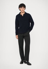 Marinblå stickad polo tröja med krage, i kombination med skräddarsydda svarta byxor och svarta skor. Slät textur, modern passform, minimalistisk design.