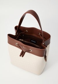 Sangkar tas dengan kulit sintetis krim dan coklat. Dilengkapi dengan perangkat keras emas, penutupan tali serut, dan kantong zip di dalam. Logo terlihat.