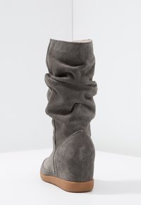 Stivaletto in camoscio grigio con tacco a cuneo e design arricciato, dotato di una parte superiore texturizzata e una suola in gomma marrone a contrasto.