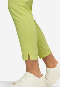 Helle limonengrüne Caprihosen aus Baumwolle, mit seitlichen Schlitzen am Saum und kombiniert mit weißen Sneakers.