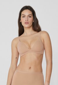 Nude bralet s hlubokým výstřihem, nastavitelné popruhy a hladkým povrchem. Lehký a bezešvý design.