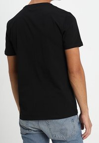 Camiseta de algodón negra de manga corta, con cuello redondo y un diseño simple y sin adornos. Se lleva con jeans de mezclilla azul claro.