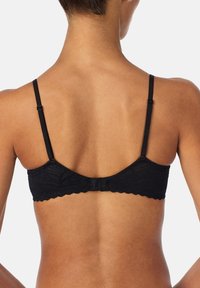 Zwarte kanten beha met gegolfde randen, verstelbare bandjes en een haak-en-oogsluiting aan de achterkant. Gladde textuur en bloemenpatroon.