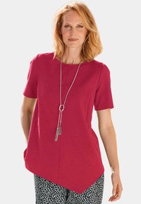 Tunic fucsia a maniche corte con orlo curvo e due tasche laterali, abbinato a pantaloni a pois. Collana d'argento a più strati in evidenza.