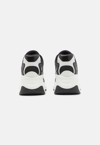 Para czarnych i białych butów sportowych widocznych od tyłu, z grubymi białymi podeszwami i wyściełanymi kołnierzami na kostkach na białym tle.