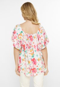 Blusa floreale con maniche corte, collo ampio e vestibilità ampia, con una combinazione di tonalità rosa, arancione e verde su uno sfondo chiaro.
