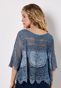 Top all'uncinetto azzurro chiaro con design a maglia aperta, orlo sagomato e ricami floreali. Presenta maniche ampie e una vestibilità rilassata.
