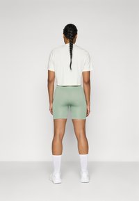 Una camiseta corta blanca y unos pantalones cortos de ciclismo de color verde menta con textura acanalada, combinados con calcetines blancos y zapatillas deportivas, vistos desde atrás.