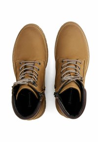 Par de botas de cuero en color marrón claro con cordones, forro interior oscuro, cuellos acolchados y costuras visibles alrededor de las suelas.