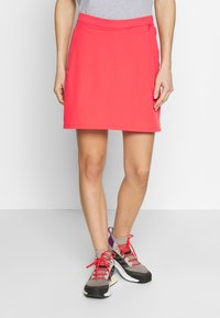 Korallrosa sportkjol med en åtsittande midja, med en slank design och mjuk textur, i kombination med grå och röda träningsskor.