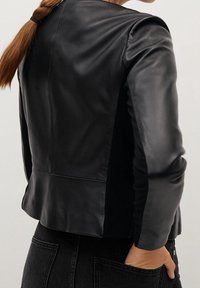 Zwarte leren jas met een getailleerd ontwerp, een gladde textuur en gestructureerde schouders. Bevat naaddetails en heeft een iets cropped lengte.