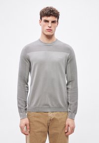 Pulover gri deschis cu mâneci lungi, cu panou texturat în partea superioară și corp neted; prezintă un decolteu rotund și un logo subtil pe piept.