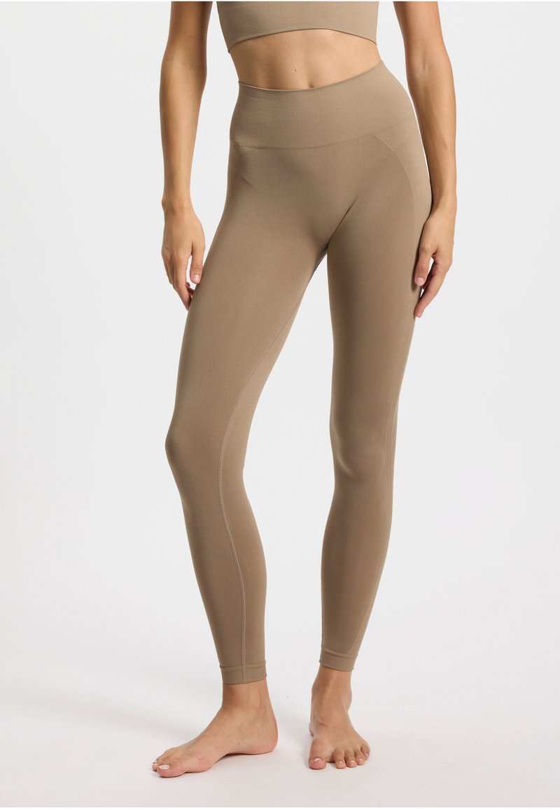 Leggings couleur sable avec une taille haute, un design sans coutures, et des coutures détaillées. Tissu doux et extensible avec une texture lisse.