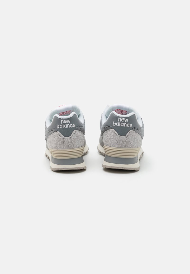 Des baskets grises avec un mélange de matériaux en maille et en suédé, dotées d'un col rembourré, d'un logo blanc et d'une semelle en caoutchouc texturée beige.