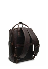 Zaino in pelle marrone scuro con spallacci imbottiti, maniglia superiore, tasche laterali e scomparti con zip, mostrato dalla parte posteriore su sfondo bianco.