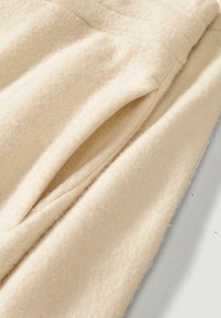 Crème-kleurige wollen stof met een zachte, gestructureerde oppervlakte, voorzien van nette plooien en een gladde afwerking.