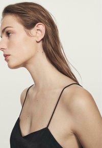Indumento senza maniche di colore nero con sottili spalline, caratterizzato da un profondo scollo a V. La texture liscia e il design aderente mettono in risalto il décolleté e le spalle.