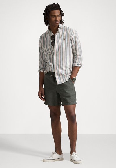Cămașă cu dungi în tonuri deschise, pantaloni scurți verzi și adidași albi. Include ochelari de soare și ceas, creând un aspect casual.