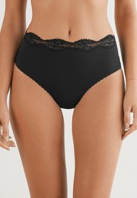 Sous-vêtements noirs taille haute en tissu côtelé, ornés d'une bordure en dentelle festonnée le long de la taille et de coutures décoratives.