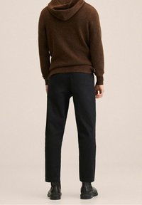 Hoodie marron en maille avec capuche, associé à un pantalon noir fuselé et des bottes noires, vu de dos sur un fond neutre.