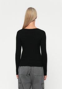 Tricou lung cu maneci din tricot negru, cu un croi ajustat, decolteu larg, textură fină, purtat cu pantaloni cargo gri, care au buzunare laterale.