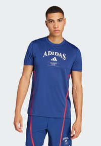 Blåt träningsskjorta med korta ärmar, vit "ADIDAS"-logotyp, röda sidor, rundad halsdesign, tillverkad av fukttransporterande tyg.