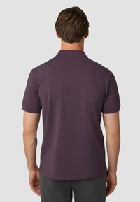 Donkerpaarse polo shirt met korte mouwen, een klassieke kraag en een klein accentdetail op de achterkant. De stof lijkt glad en textuur te hebben.