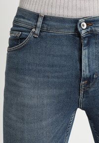 Slim fit blå denimjeans med en blekt textur, utrustade med framfickor, dragkedja och knappstängning i midjebandet.