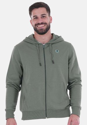 Haut à capuche zippé vert olive en tissu doux, doté d'une capuche, de poches avant et d'un petit logo sur la poitrine gauche. Texture lisse.