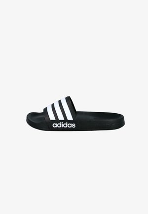 Sandalia tipo slide negra de Adidas con tres franjas blancas y el logo de Adidas en la correa, mostrada de lado sobre un fondo blanco.