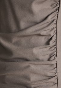 Staubgrauer Stoff mit geraffter Textur. Glattes, leicht dehnbares Material erzeugt weiche Falten entlang der Kante. Keine sichtbaren Muster oder Beschläge.
