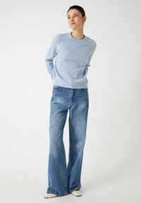 Hellblauer Strickpullover mit Rundhalsausschnitt und gerippten Bündchen, kombiniert mit hoch taillierten blauen Denim-Weitbeinform-Jeans. Glatte Textur, lässige Passform.
