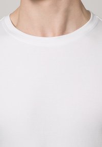 Camiseta de algodão branca com decote redondo, design sem costuras e textura suave, apresentando uma vista aproximada da gola e da área do peito.