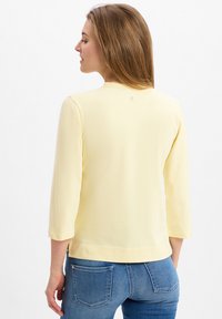Yellow long-sleeve top with a rounded neckline and side slits, made from a soft material, features a small logo detail on the back.